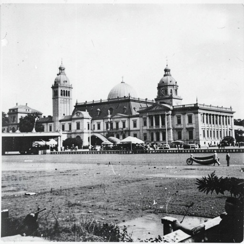 Warm-toned duotone photograph of a stately heritage building facade in Bombay, featuring arched windows and stone columns in deep brown and cream tones.
